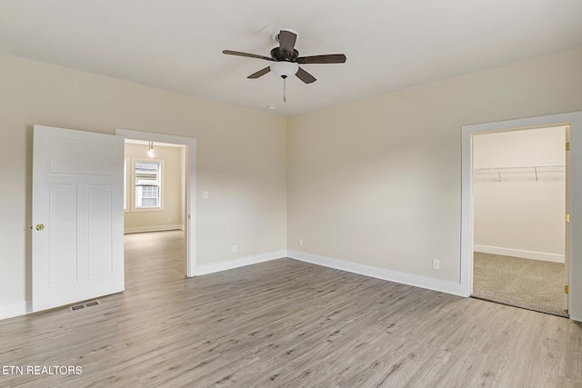 unfurnished bedroom with a closet, a spacious closet, ceiling fan, and light hardwood / wood-style floors