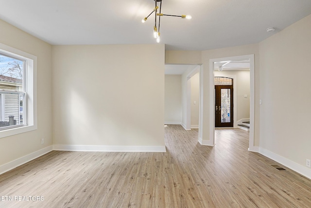 empty room with a notable chandelier and light hardwood / wood-style floors