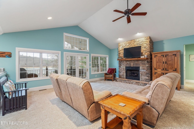 living room featuring a stone fireplace, ceiling fan, light colored carpet, and a wealth of natural light