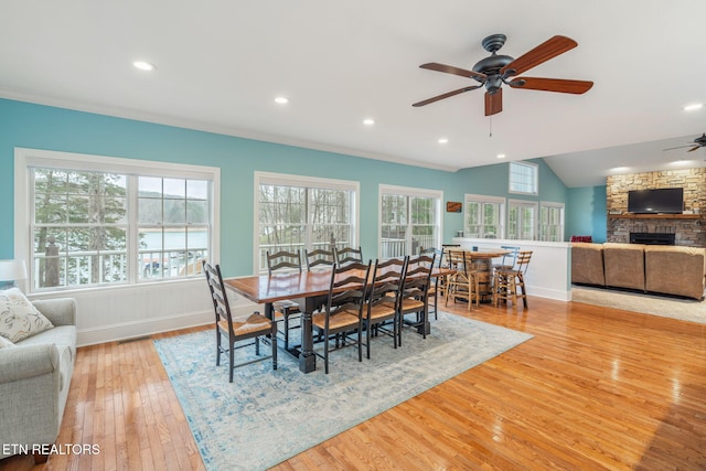 dining room with ceiling fan, a fireplace, light hardwood / wood-style floors, and lofted ceiling