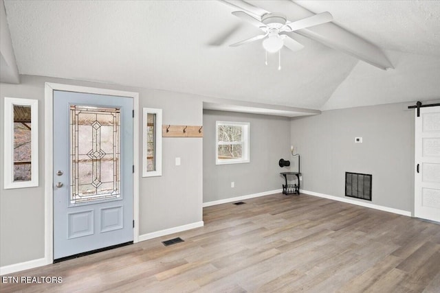 entryway featuring ceiling fan, a barn door, lofted ceiling, and light hardwood / wood-style flooring