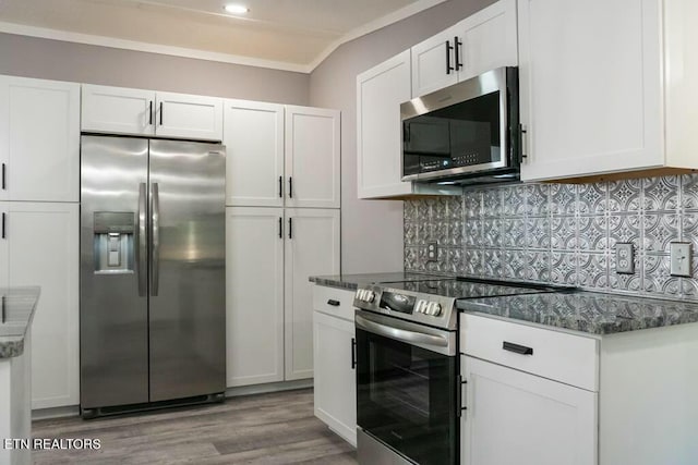 kitchen featuring stainless steel appliances, dark stone countertops, hardwood / wood-style floors, decorative backsplash, and white cabinets