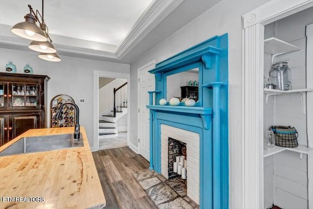 bar with a brick fireplace, wooden counters, decorative light fixtures, hardwood / wood-style flooring, and ornamental molding