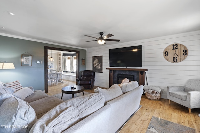 living room with light hardwood / wood-style flooring, ceiling fan, crown molding, and wood walls