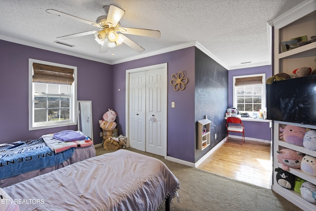 bedroom with carpet flooring, ceiling fan, a textured ceiling, a closet, and ornamental molding