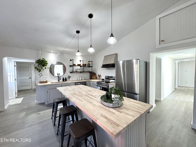 kitchen with sink, appliances with stainless steel finishes, decorative light fixtures, light hardwood / wood-style floors, and custom range hood