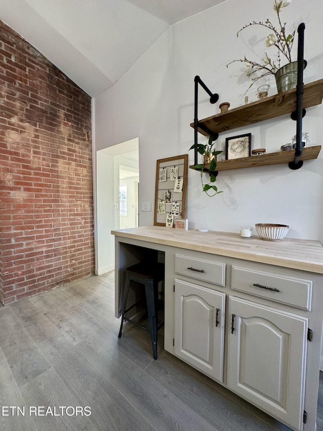 bar featuring light hardwood / wood-style floors, vaulted ceiling, and brick wall