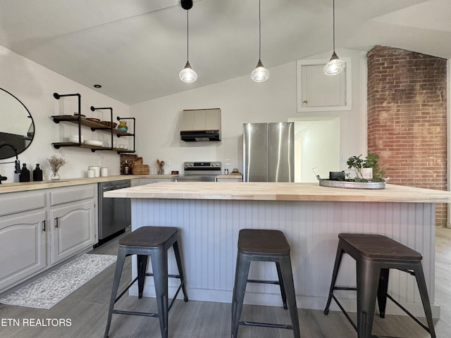 kitchen with a center island, stainless steel appliances, butcher block countertops, wood-type flooring, and a breakfast bar area