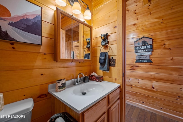 bathroom with vanity, wooden walls, and toilet