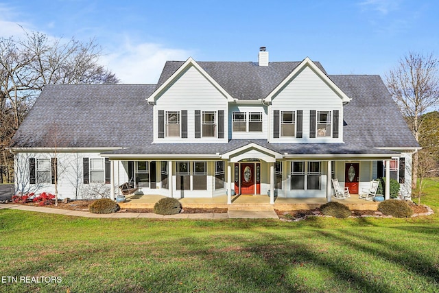 traditional-style house featuring a front yard, covered porch, roof with shingles, and a chimney