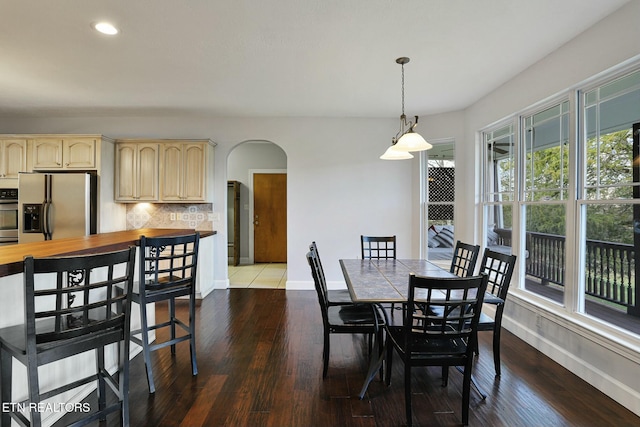 dining room featuring arched walkways, wood finished floors, and baseboards