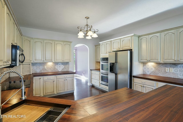kitchen with arched walkways, stainless steel appliances, butcher block counters, and cream cabinetry