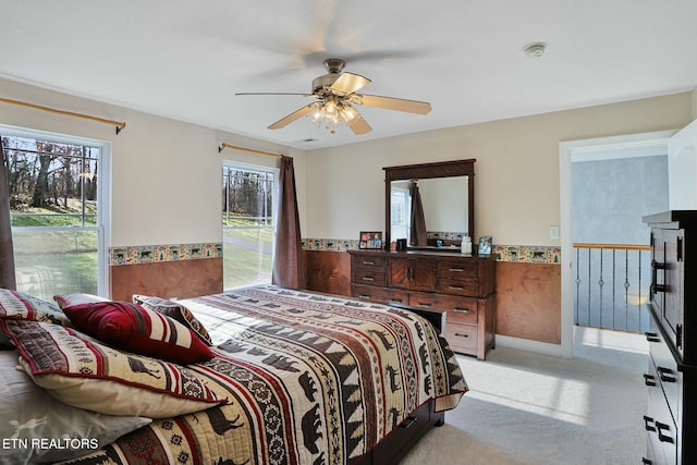 bedroom featuring light carpet, ceiling fan, and wainscoting