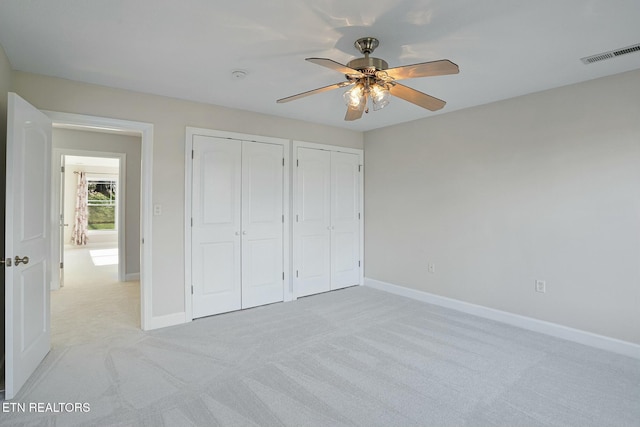 unfurnished bedroom featuring two closets, visible vents, light carpet, ceiling fan, and baseboards