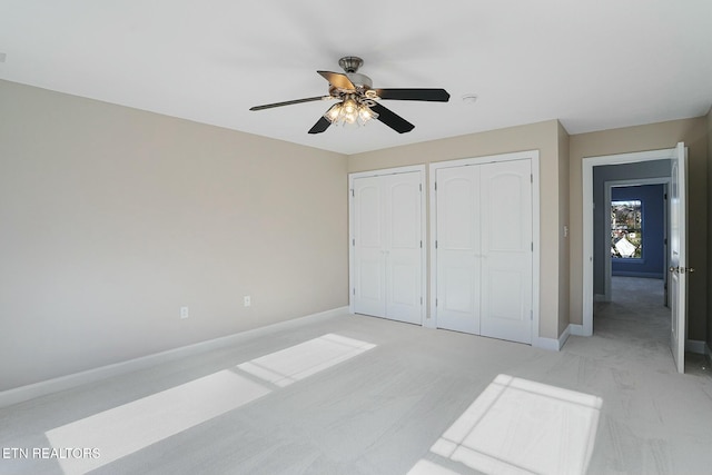 unfurnished bedroom with light carpet, ceiling fan, baseboards, and two closets