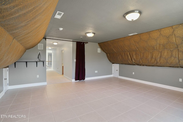additional living space featuring visible vents, vaulted ceiling, a textured ceiling, and baseboards