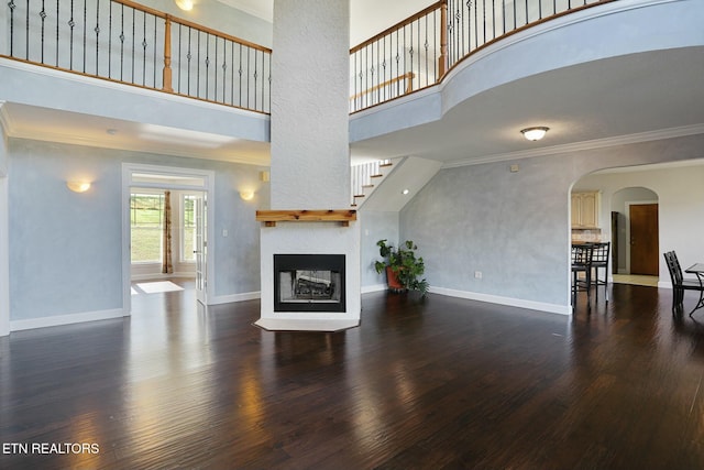 unfurnished living room featuring ornamental molding, dark wood-type flooring, a multi sided fireplace, and baseboards