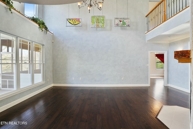 unfurnished room with an inviting chandelier, baseboards, a high ceiling, and wood finished floors