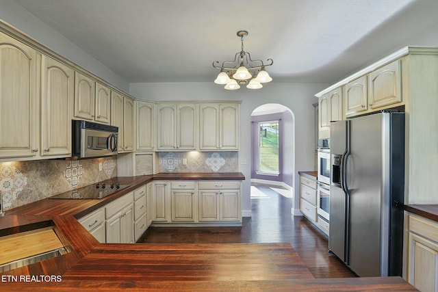 kitchen featuring stainless steel appliances, cream cabinets, dark countertops, and decorative light fixtures