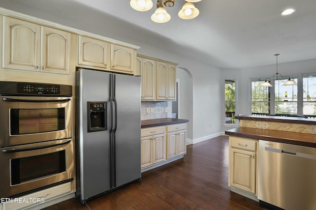 kitchen featuring arched walkways, pendant lighting, dark wood finished floors, stainless steel appliances, and backsplash