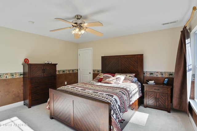 bedroom featuring light carpet, a wainscoted wall, ceiling fan, and visible vents