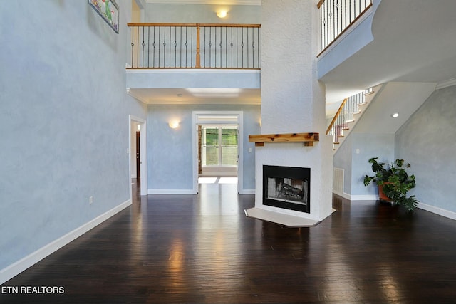 unfurnished living room featuring dark wood-style floors, a glass covered fireplace, a towering ceiling, and baseboards