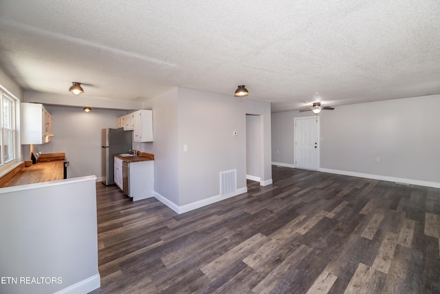 unfurnished living room with ceiling fan, dark hardwood / wood-style flooring, and a textured ceiling