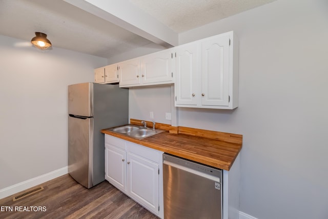 kitchen with a textured ceiling, stainless steel appliances, sink, butcher block countertops, and white cabinetry