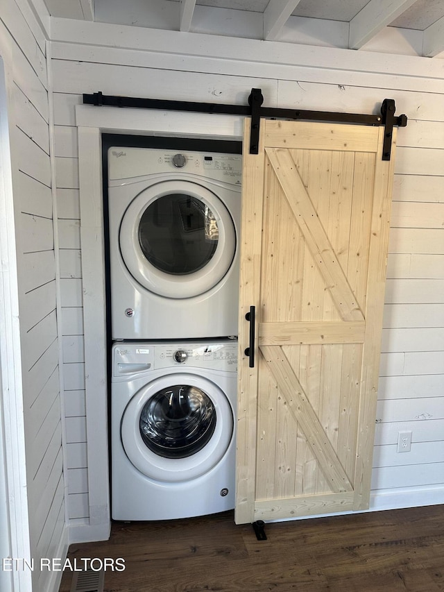 clothes washing area featuring a barn door, stacked washer and dryer, dark wood-style flooring, and laundry area