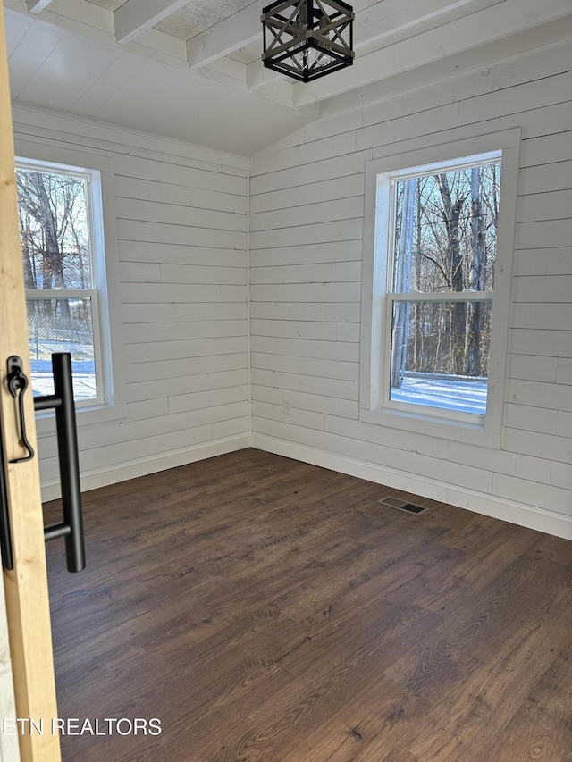 spare room featuring dark wood finished floors, beamed ceiling, plenty of natural light, and visible vents