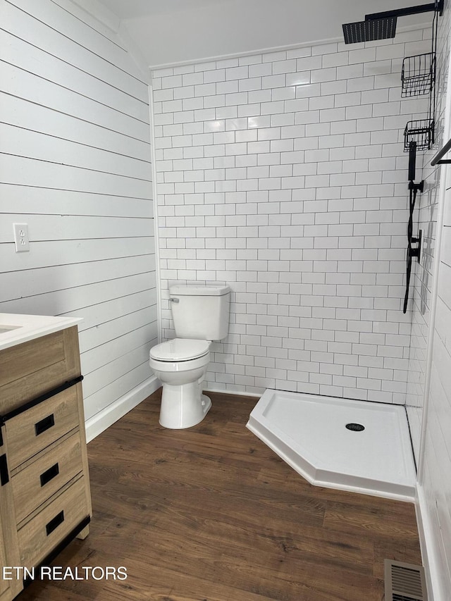 bathroom with a tile shower, vanity, hardwood / wood-style flooring, toilet, and lofted ceiling