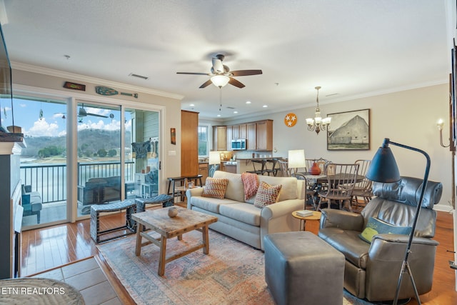 living room with ceiling fan with notable chandelier, light hardwood / wood-style floors, and crown molding