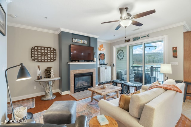 living room featuring ceiling fan, light hardwood / wood-style floors, crown molding, and a tile fireplace