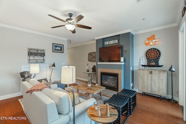 living room with hardwood / wood-style floors, ceiling fan, crown molding, and a tiled fireplace