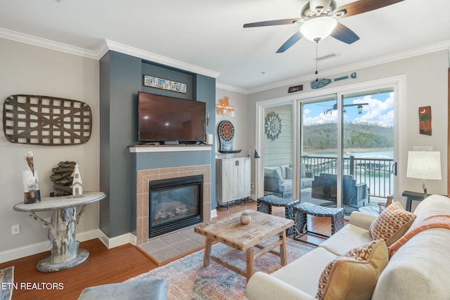 living room with ceiling fan, a fireplace, ornamental molding, and hardwood / wood-style flooring