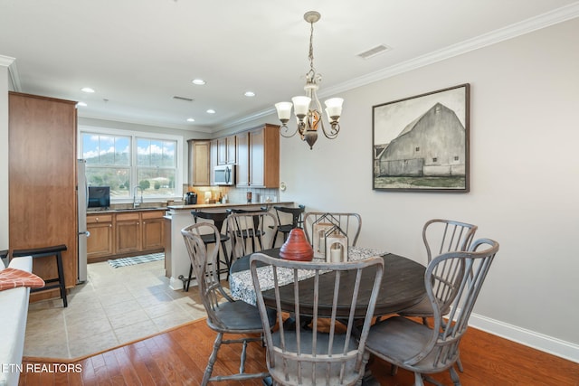 dining space with sink, ornamental molding, a chandelier, and light hardwood / wood-style floors