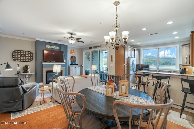 dining room featuring a tile fireplace, a healthy amount of sunlight, crown molding, and light hardwood / wood-style floors