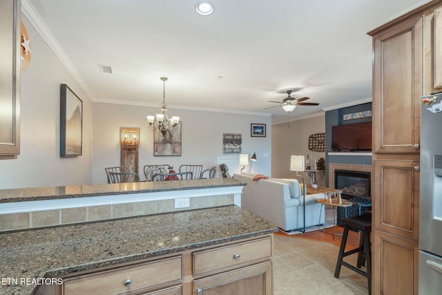 kitchen with a breakfast bar, ceiling fan with notable chandelier, stainless steel fridge, dark stone countertops, and ornamental molding