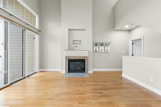 unfurnished living room featuring a tiled fireplace, a towering ceiling, a healthy amount of sunlight, and light wood-type flooring