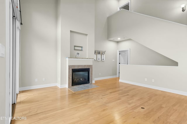 unfurnished living room featuring a tiled fireplace, a high ceiling, and light wood-type flooring