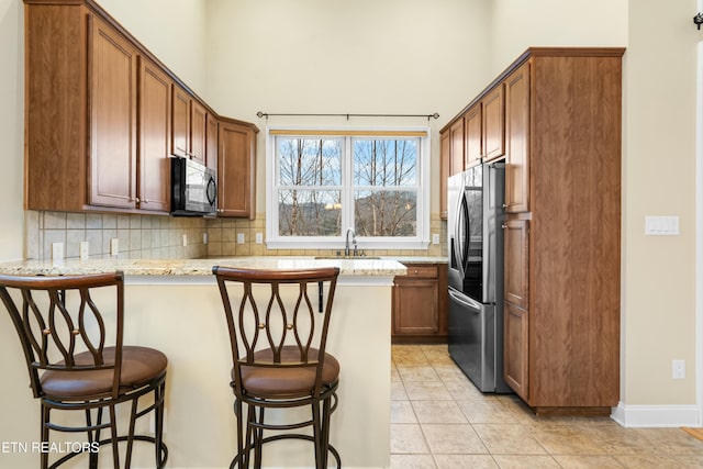 kitchen featuring decorative backsplash, stainless steel fridge, kitchen peninsula, light stone counters, and a breakfast bar area