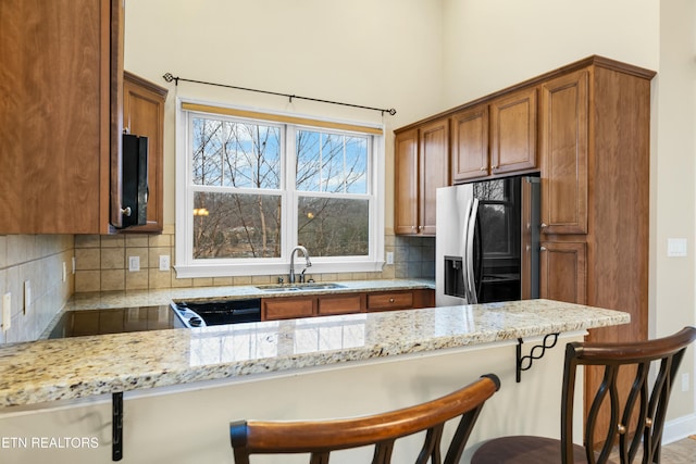 kitchen featuring light stone countertops, sink, stainless steel fridge with ice dispenser, kitchen peninsula, and a breakfast bar