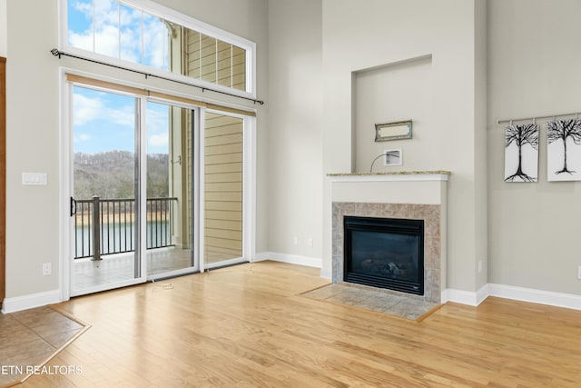 unfurnished living room featuring wood-type flooring, a towering ceiling, and a tiled fireplace