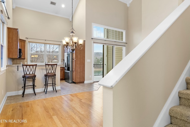 staircase featuring wood-type flooring, an inviting chandelier, ornamental molding, and a high ceiling