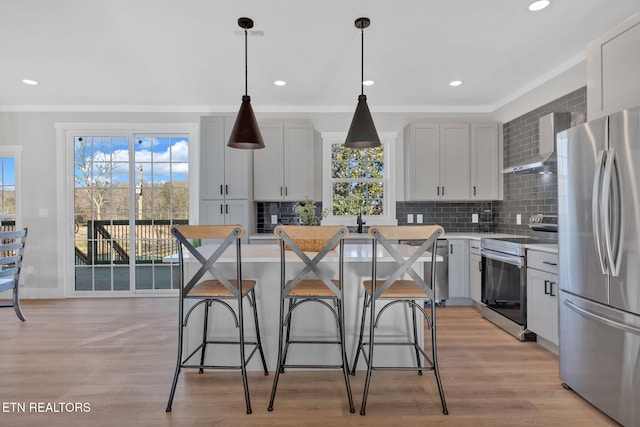 kitchen featuring stainless steel appliances, a kitchen island, wall chimney range hood, and hanging light fixtures