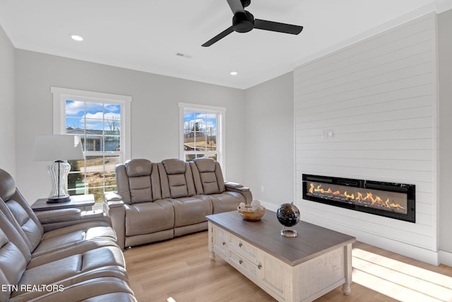 living room with a large fireplace, ceiling fan, and light wood-type flooring