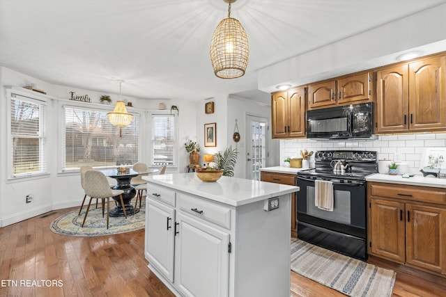 kitchen featuring pendant lighting, backsplash, black appliances, white cabinets, and light hardwood / wood-style floors