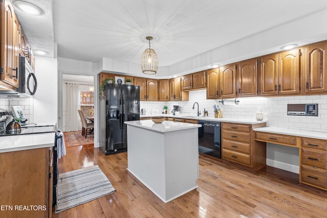 kitchen with sink, light hardwood / wood-style flooring, pendant lighting, a kitchen island, and black appliances