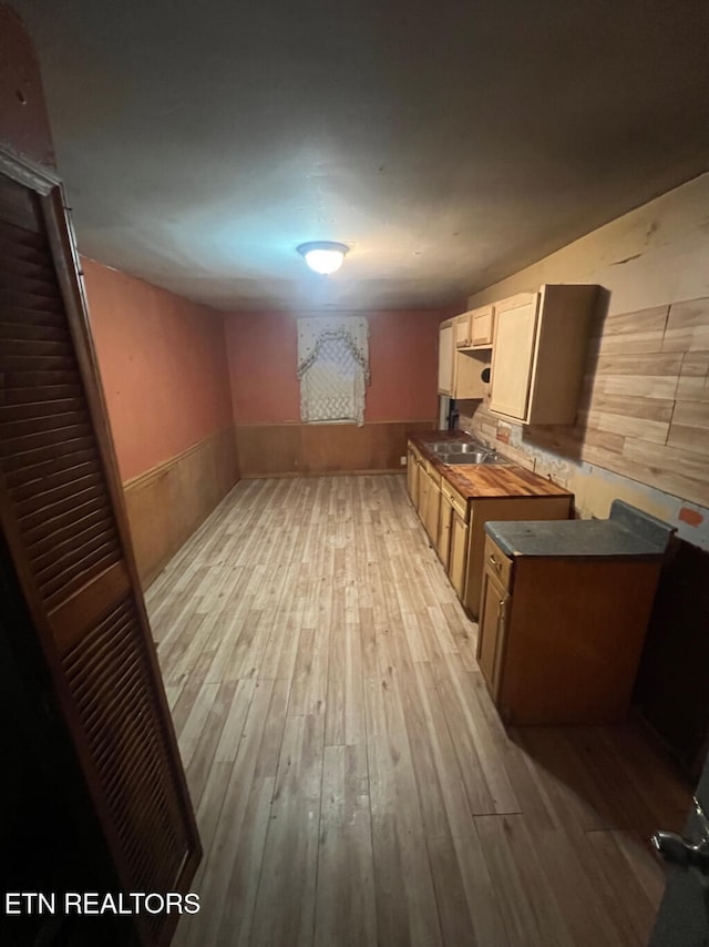 kitchen with sink, light hardwood / wood-style flooring, wooden counters, wooden walls, and white cabinets