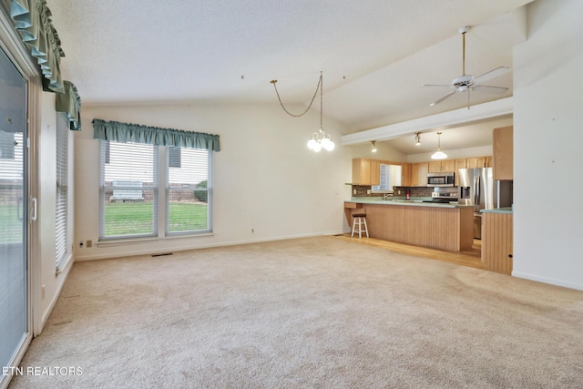 unfurnished living room with ceiling fan with notable chandelier, light colored carpet, and vaulted ceiling